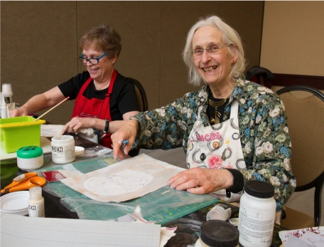 Two women at a table,  smiling while surrounded by art supplies